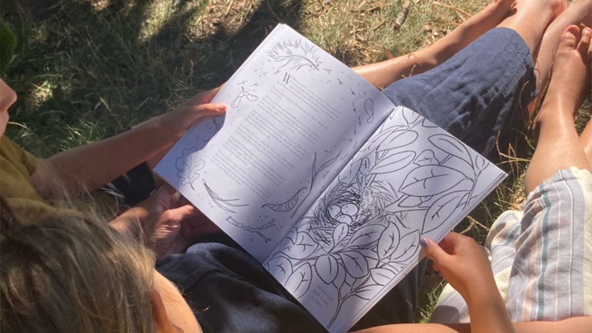 Parent and child sitting in the grass reading the Beautiful Words coloring book, showcasing a lifestyle view of the book in use.