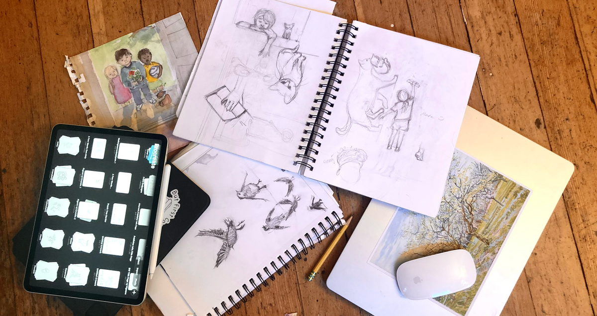 Sketchbooks and digital tools used for the Beautiful Words coloring book spread across a wooden work table